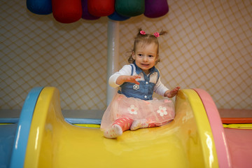 Happy little kid girl play in the playing room sliding off the slide. Funny child having fun indoors. Birthday party