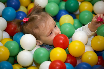 Fototapeta na wymiar Happy little kid girl play in the playing room pool full of colorful balls. Funny child having fun indoors. Birthday party