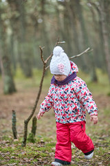 Little girl wear jacket and hat walk is playing at the forest near baltic sea on cloudy sky in winter time.