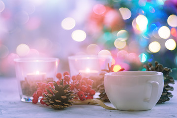 Still life with a cup. Christmas tree in the back. Colorful light bulbs. Light background