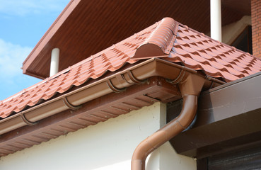 Close up on roof gutter holder and guttering downspout pipe with clay tiles roof. Installing rain...