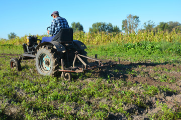 Obraz premium Farmer on old handmade tractor plowing. Farmer Tractor.