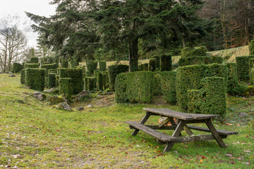 Mesa de picnic junto a un gran árbol y unos arbustos podados con diferentes formas, área de descanso del Pirineo Francés
