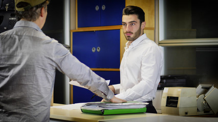 Businessman standing at office desk and looking at paper file full of documents given to him by unrecognizable employee or boss