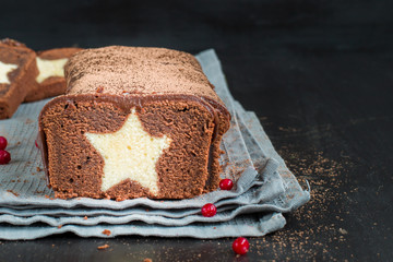 A very chocolate cake covered with dark chocolate and sprinkled with cocoa with a vanilla star inside. On a wooden dark background. Decorated with fresh cranberries, The perfect cool Christmas dessert