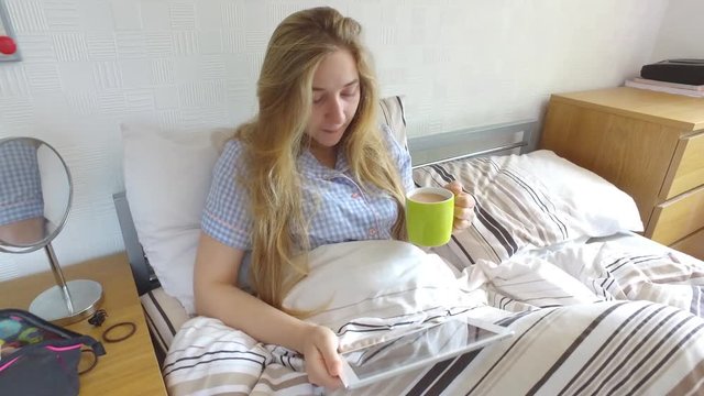 Authentic shot of beautiful girl in bed watching her tablet while enoying a hot cuppa tea