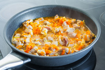 Meat with vegetables is stewed in a frying pan