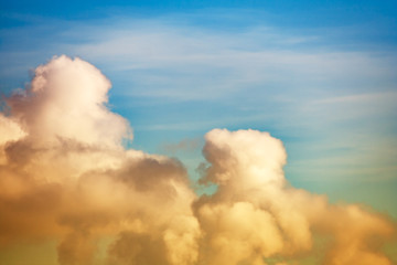 Orange fluffy clouds illuminated by sunlight against a blue sky (background)