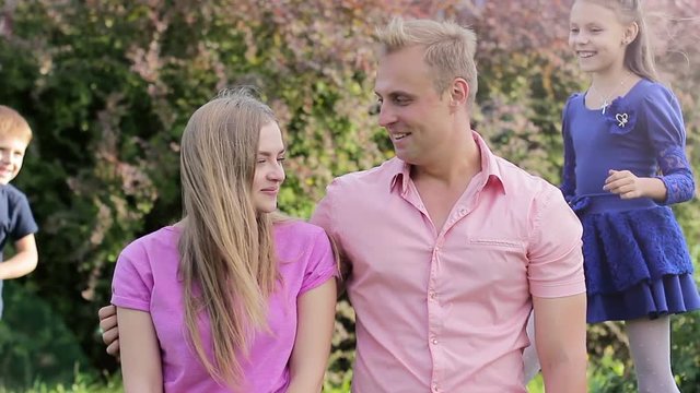 Little children love their young parents. Young family having fun together outdoors in the garden. The concept of a fun and friendly family