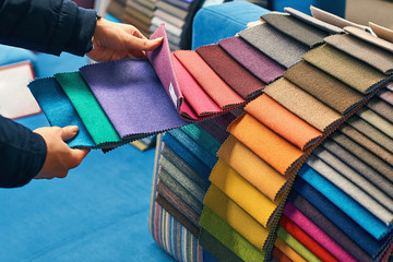 Young woman is making her decision while choosing a color of a fabric from a huge variety in a shop