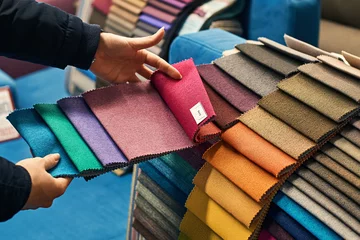 Gordijnen Jonge vrouw neemt haar beslissing terwijl ze een kleur van een stof kiest uit een enorme variëteit in een winkel © berezko