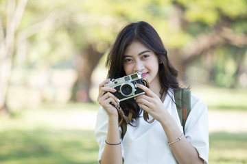 Attractive Asian woman holding retro camera with smiling, Woman using camera at outdoor place.