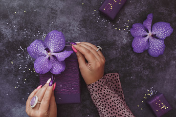 Female hands with perfect manicure wrapping gifts and decorating with orchid flowers, holiday concept. Top view, blank space