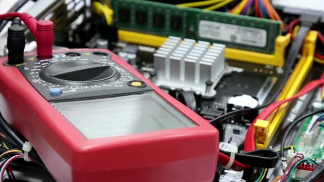 Red  multimeter for repair equipment, selective focus with shallow depth of field. Measurement of the voltage in the motherboard.
