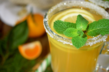 Yellow cocktail in a glass mug decorated with sugar border and mint surrounded by Christmas attributes