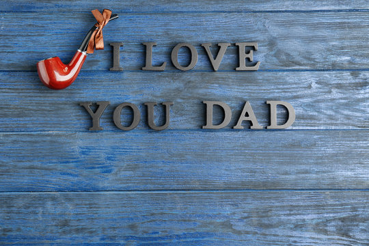 Words "I love you dad" and tobacco pipe on blue wooden background