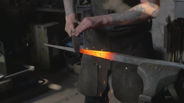Blacksmith using file to smooth down heated metal, sparks fly