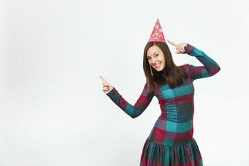 Beautiful caucasian young woman in plaid dress and birthday party hat with charming smile, celebrating holiday pointing two fingers away at copy space isolated over white background for advertisement.