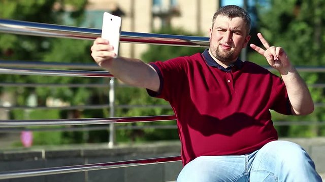 Man in red shirt makes selfie. Man makes photos on his smartphone