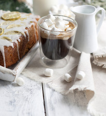 a glass with coffee and small marshmallow, a cupcake and a branch of a Christmas tree, on a white wooden background