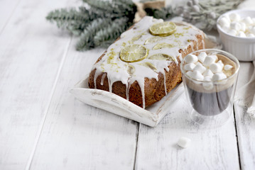 a glass with coffee and small marshmallow, a cupcake and a branch of a Christmas tree, on a white wooden background
