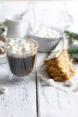 a glass with coffee and small marshmallow, a cupcake and a branch of a Christmas tree, on a white wooden background