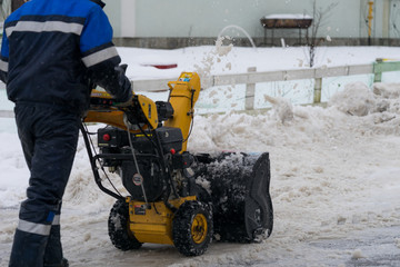 Man is cleaning the snow by the snowplow on a small street in a cottage village.  St.Petersburg,...