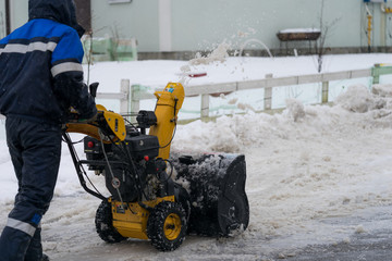 Man is cleaning the snow by the snowplow on a small street in a cottage village.  St.Petersburg,...