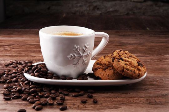 Coffee cup with chocolate cookies and coffee beans on wooden background