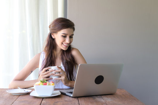 Woman having coffee and working outside. Working on laptop during her vacation in a tropical hotel. White female with white dress. Agile. modile office concept.