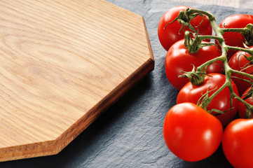 Fresh tomatoes on a branch with the cutting board on a dark background