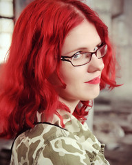 Young woman in glasses with red hair in a camouflage jacket