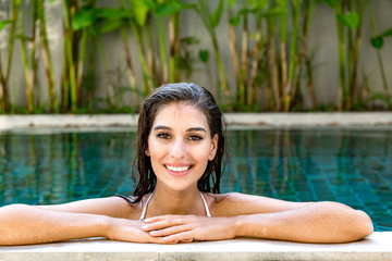 Beautiful young single white woman in pool. Relaxing in pool, wearing white bikini. Connected world concept.