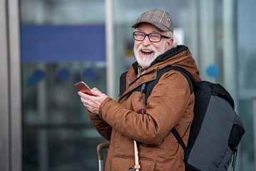 Fanny moments. Laughing old gray-haired man with beard is standing outdoors with backpack and...