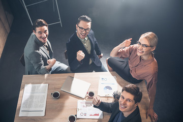 Top view portrait of happy woman and glad men raising hands up while locating at desk in apartment....
