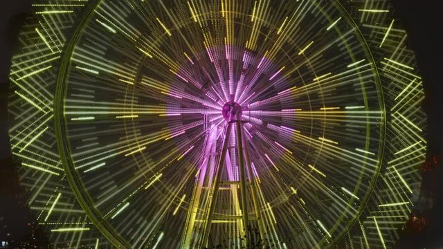 The time-laps of the Ferris wheel rotates and leaves behind a luminous trace from the colored lights.