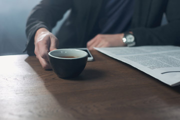 Close up man hand holding cup of delicious tea while sitting at table. Relax and business concept. Copy space