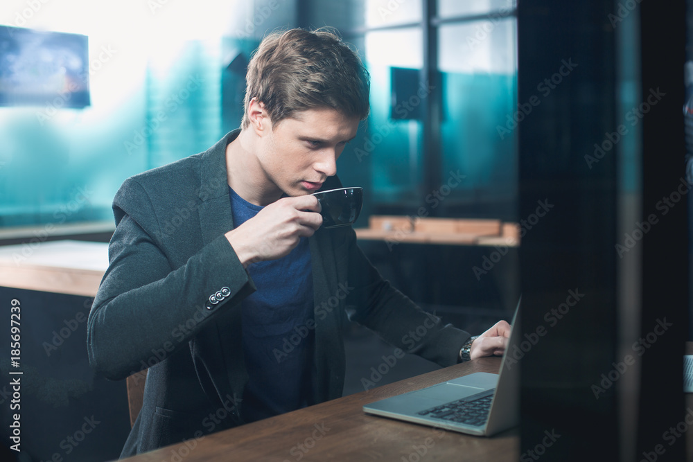 Aufkleber side view orderly male tasting appetizing cup of coffee while working at notebook computer in apartm