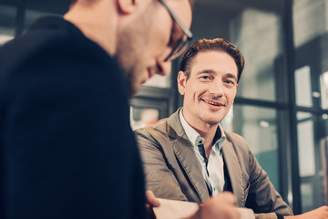 Low angle portrait of smiling businessman speaking with calm partner in office. Profession concept