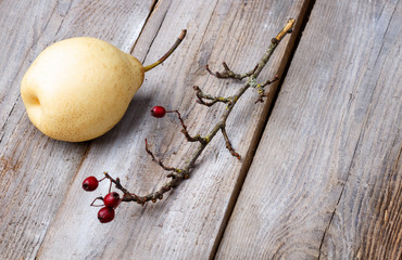 branches with red berries and pear on a wooden background