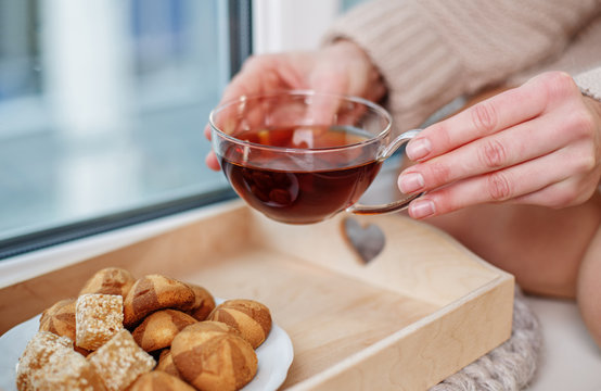 Tasty breakfast. Close up of female hands taking cup of black tea. Delicious cookies are on tray