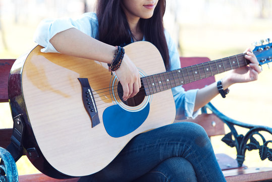 A young girl is playing guitar and sing a song in grass field at relax day with sun light.