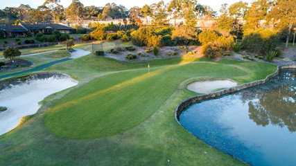 Aerial view of golf course green with flag, bunkers and dam water hazards surrounded by trees in...