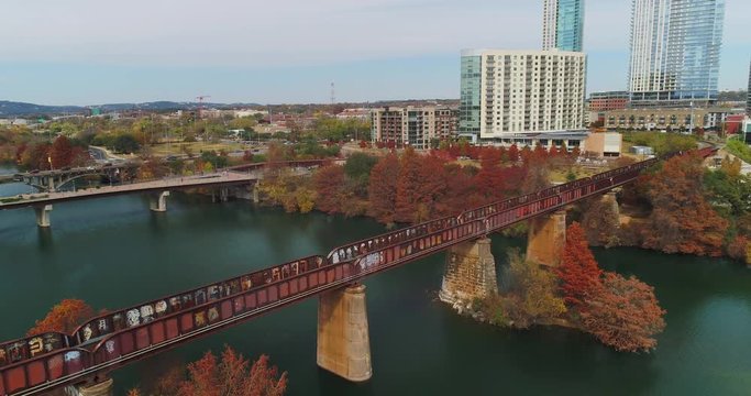 A high angle daytime exterior establishing shot of the skyline of Austin, Texas with a railroad bridge over the Colorado River in the foreground.  	
