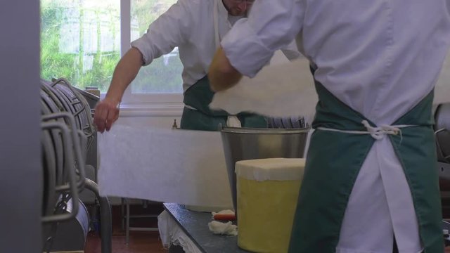Two men working in cheese making factory applying cloth to the cheeses