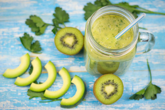Avocado smoothie with kiwi and banana and two halves of a kiwi on blue wooden table. Diet vegetarian food. Raw foods.