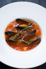 Close-up of tomato soup with mussels served in a white plate, selective focus, vertical shot