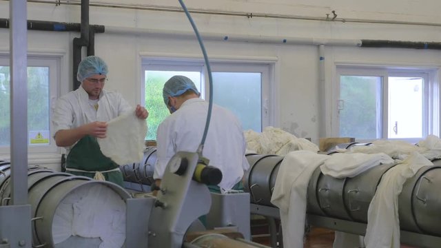 Two cheese factory employees add cloth to a cheese wheel