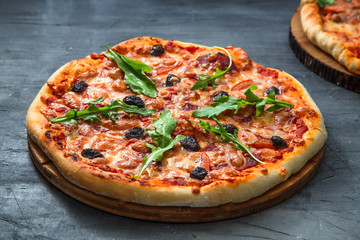 Homemade pizza with tomato, salumi, arugula and olives. Dark background