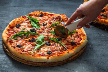 People Hands cutting homemade pizza with tomato, salumi, olives and arugula